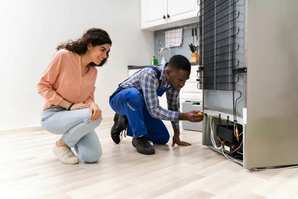 A technician performs fridge repairs for a happy customer in a kitchen