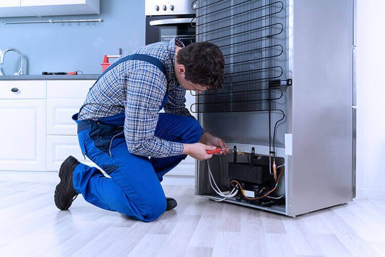 A skilled technician working on fridge repairs behind the appliance