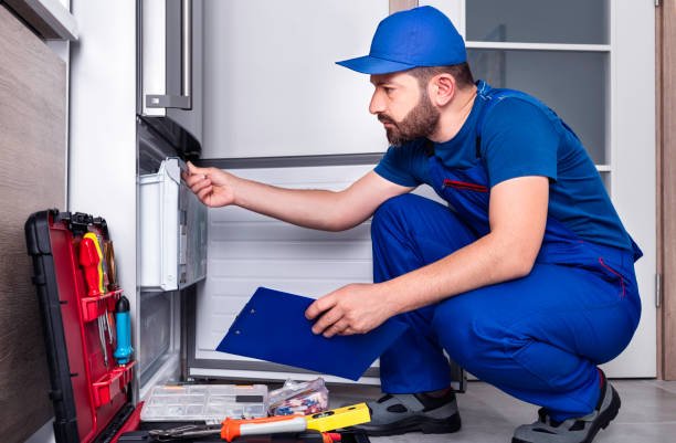 A man in a blue uniform inspecting a fridge for fridge repairs