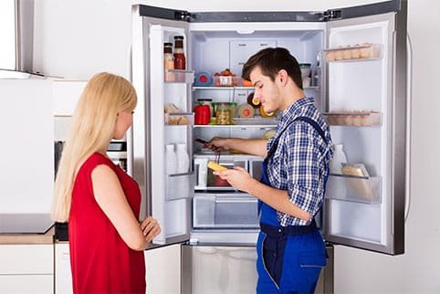 Technician performs fridge repairs on a refrigerator with a customer present